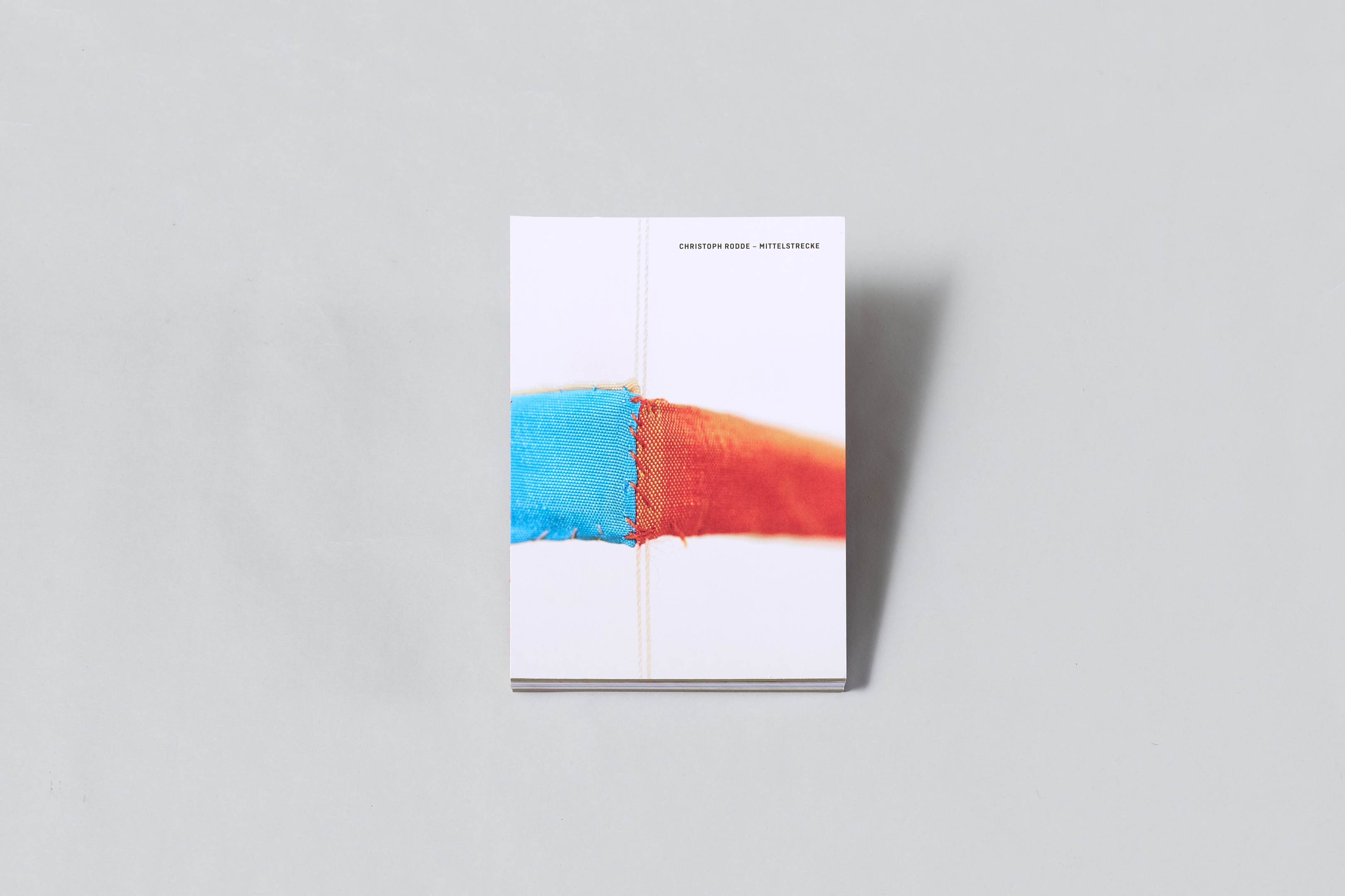 AI generated: The image shows a book with a cover featuring a close-up section of two strips of fabric sewn together in blue and red. The title "Mittelfinger" by Christoph Roehe can be seen at the top of the cover.