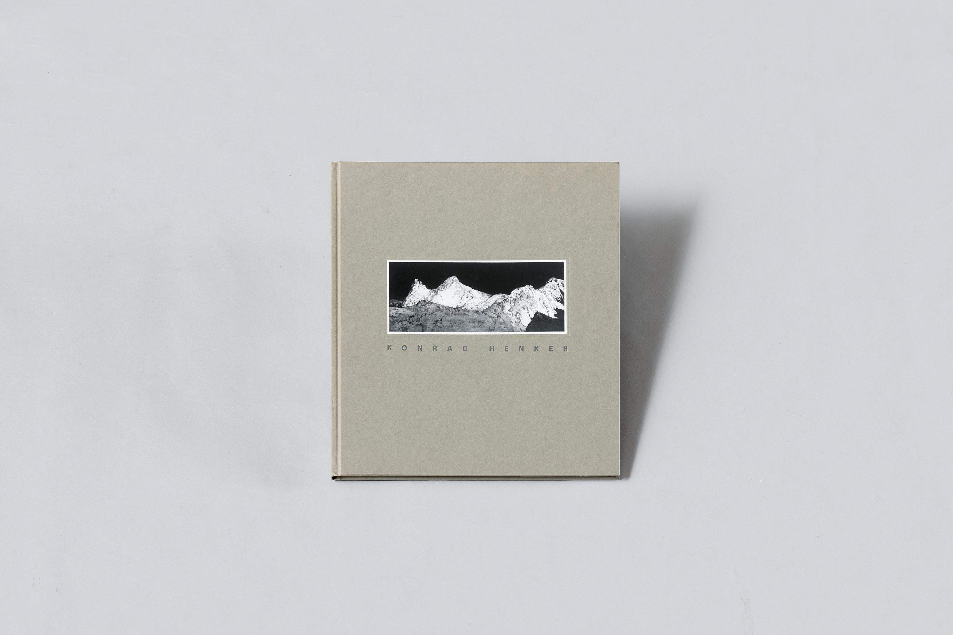 AI generated: The image shows a book with a grey cover and a centrally placed black and white photo of a mountain landscape. The name "Konrad Henker" is printed below the photo.