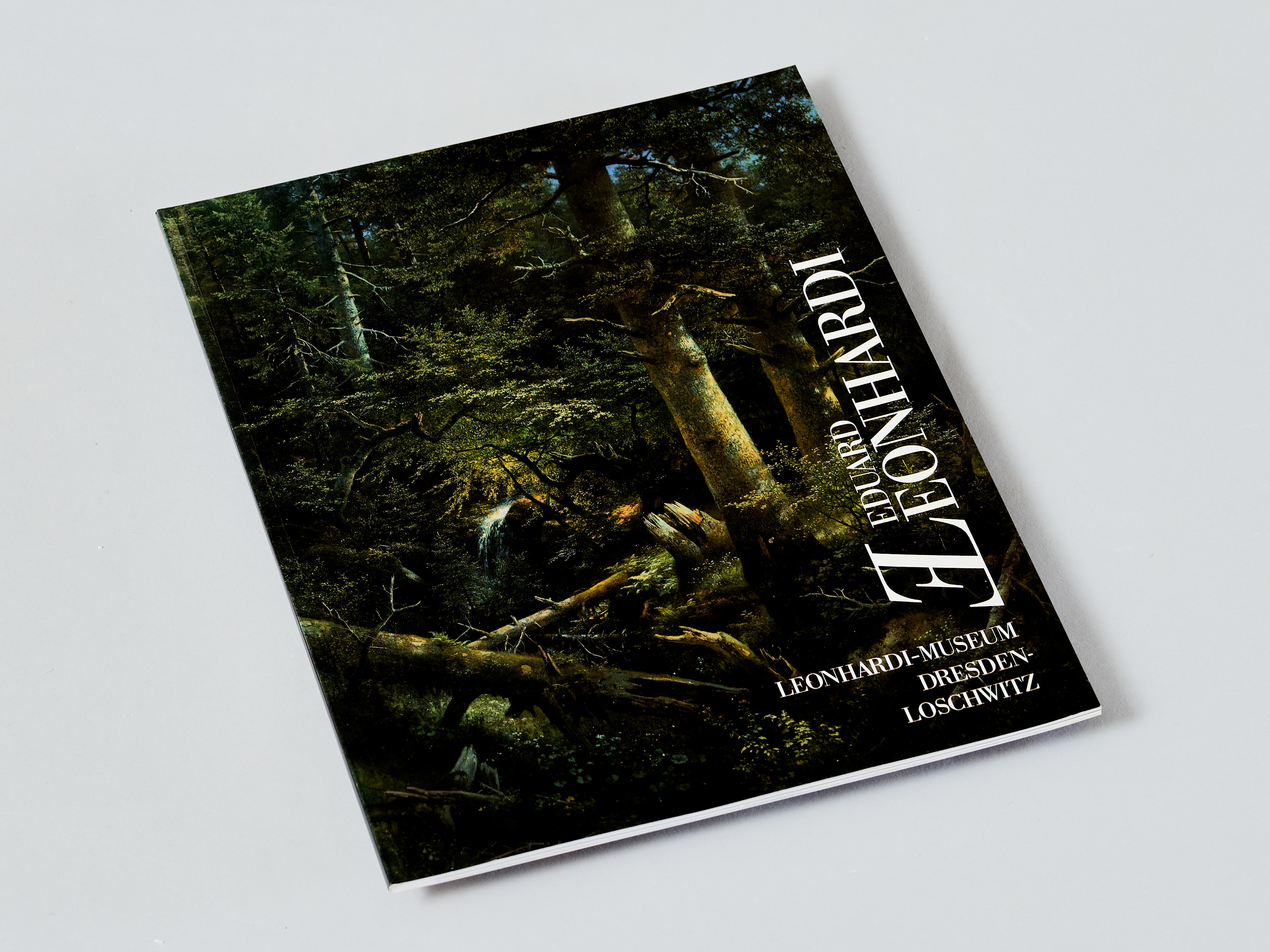 KI generiert: Das Bild zeigt ein kleines Buch oder eine Broschüre mit einem dunkelgrünen, waldähnlichen Cover-Design, das auf einem neutralen Hintergrund liegt. Auf dem Cover steht "LEONARDI."