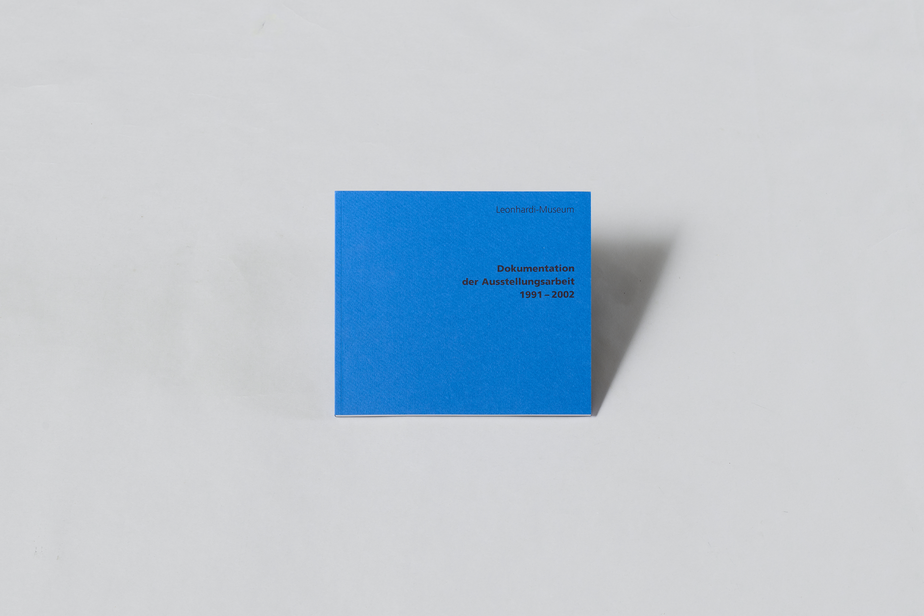 AI generated: The image shows a blue book with the title "Documentation of the exhibition work 1991-2002". It is lying on a light-coloured surface.