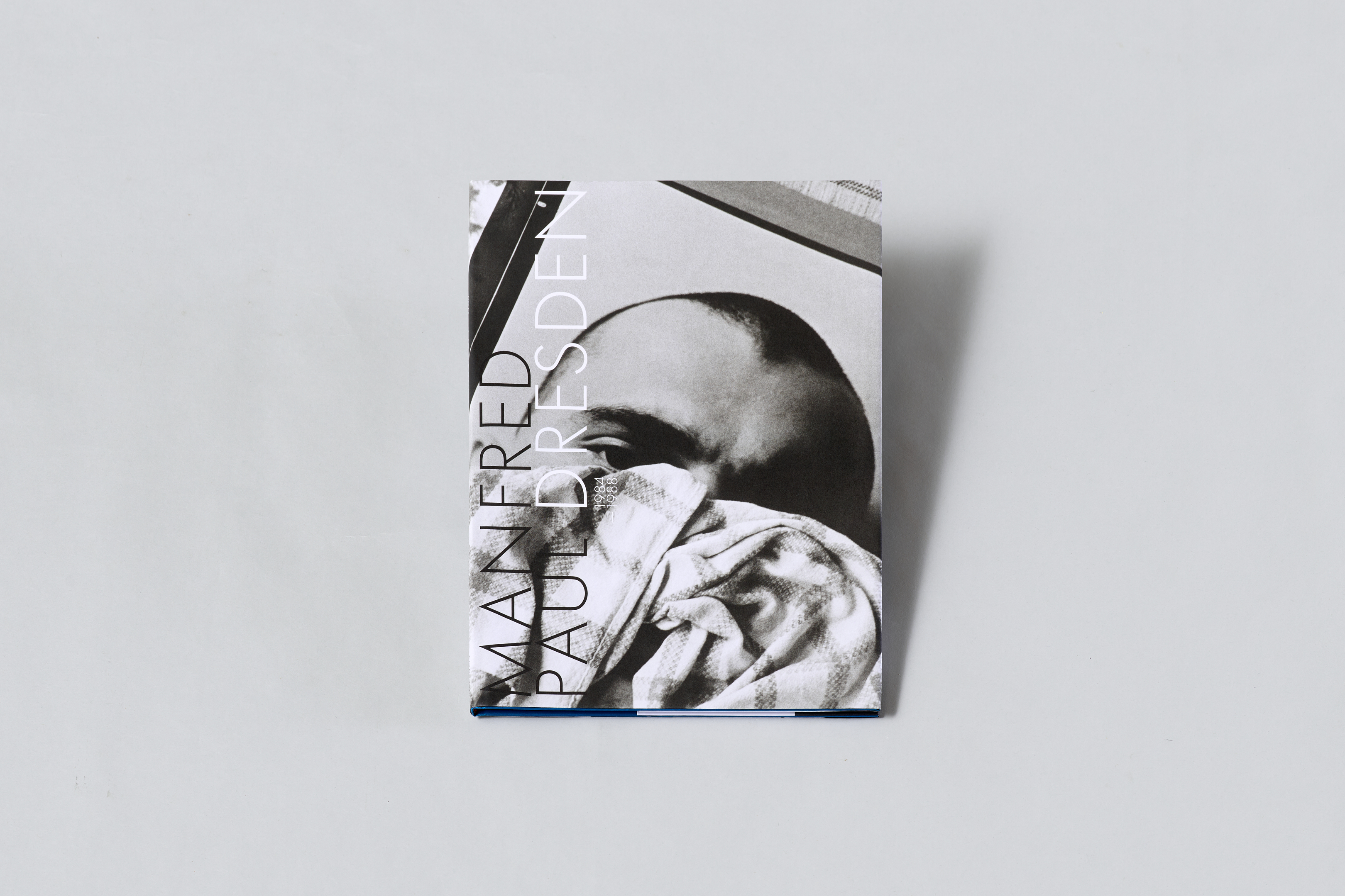 AI generated: The image shows a book cover with a black and white photograph in which a person is partially hidden behind a cloth. The title of the book "MANFRED PAUL DRESDEN" is placed diagonally on the cover.