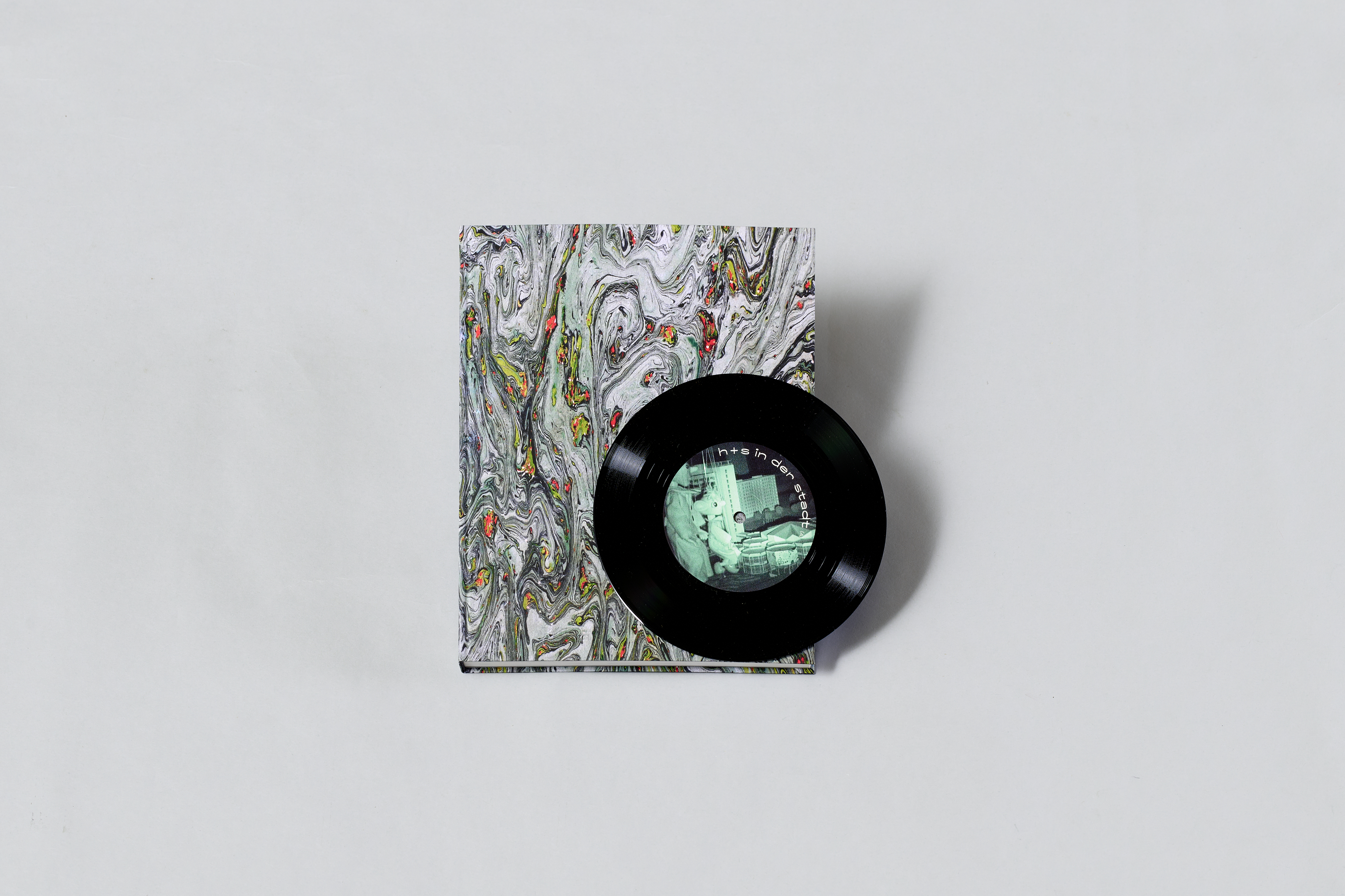 AI generated: The image shows a book with a colourful marble pattern on the cover and a small black vinyl record on it. The record has a picture in the centre that appears to show a scene with a person.