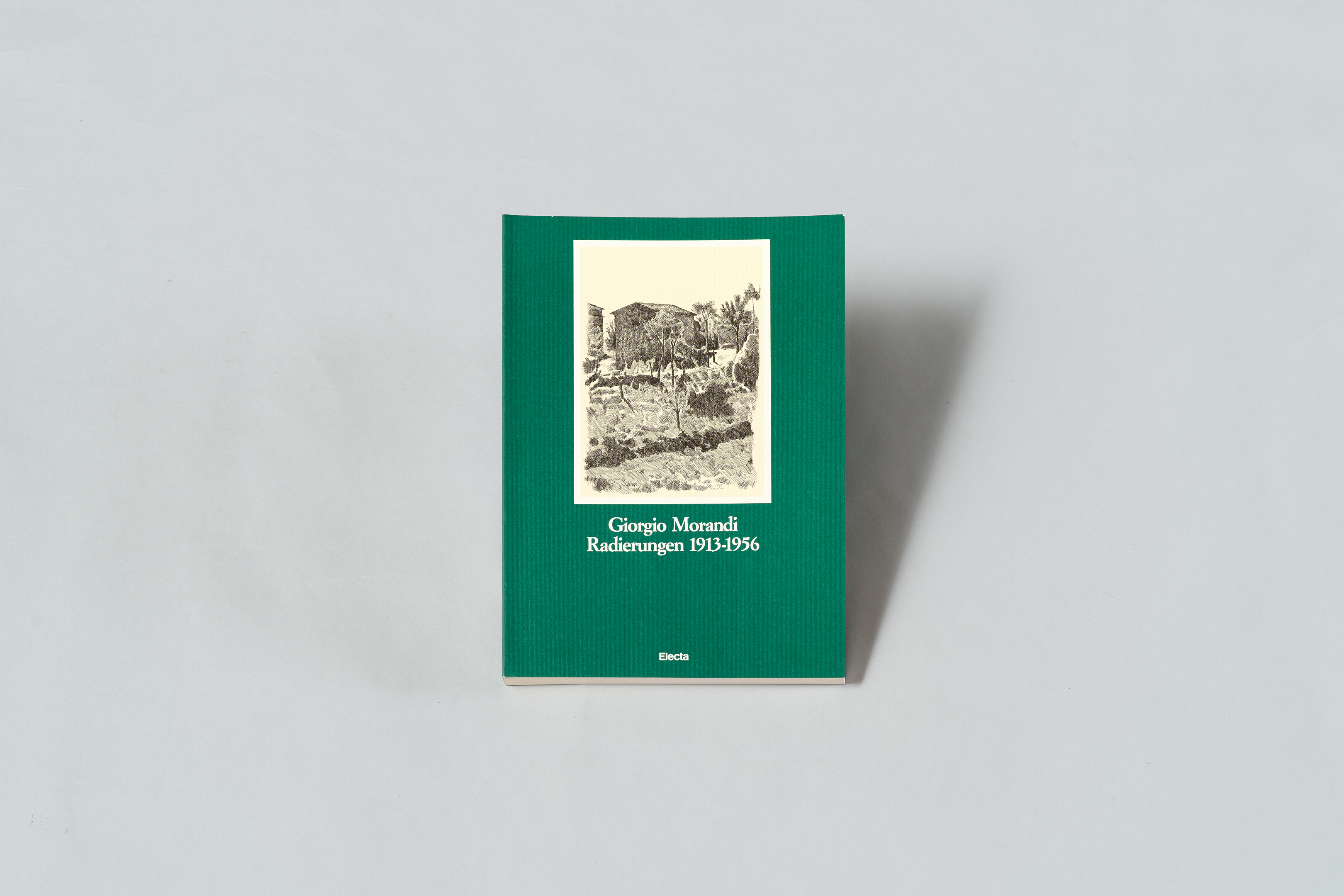 AI generated: The image shows a book with a green cover, on which a black and white image can be seen in the centre. The title of the book is "Giorgio Morandi Etchings 1913-1956".