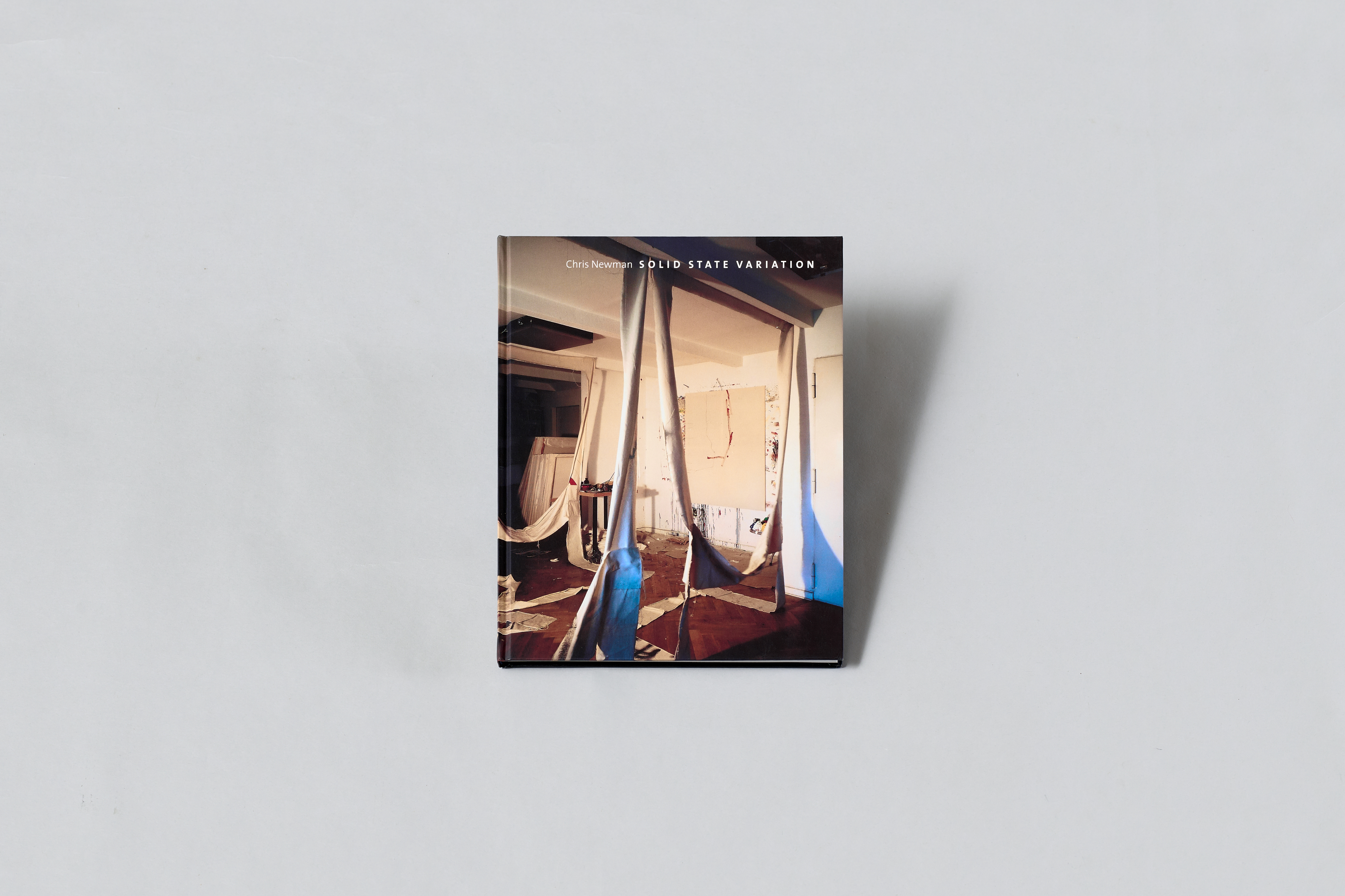 AI generated: The picture shows the book "Solid State Variation" by Chris Newman. An artistic spatial installation with cloths can be seen on the cover.