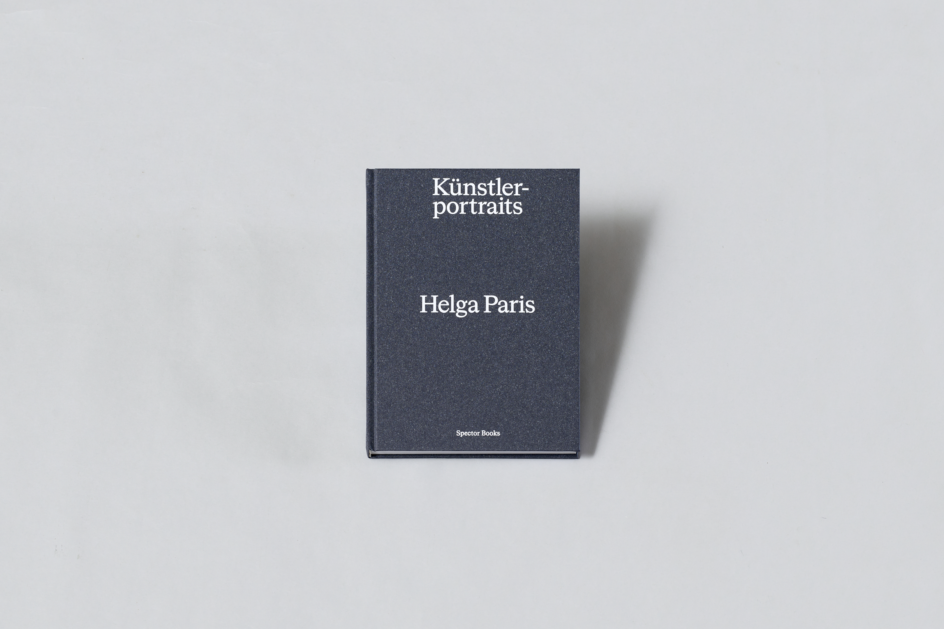 AI generated: The image shows a book entitled "Künstlerportraits" by Helga Paris lying on a grey surface. The book has a plain, dark blue cover with white lettering.