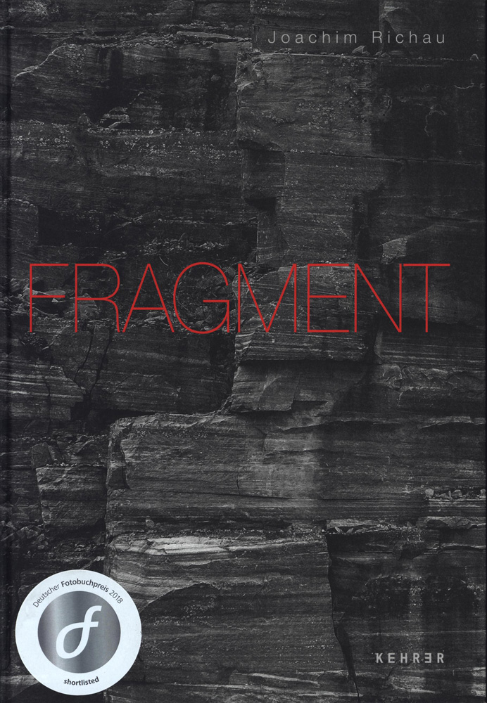 KI generiert: Das Bild zeigt das Cover eines Buches mit dem Titel "FRAGMENT" von Joachim Richau, das dunkle Gesteinsformationen im Hintergrund und einen Aufkleber des Deutschen Fotobuchpreises 2018 im Vordergrund zeigt.