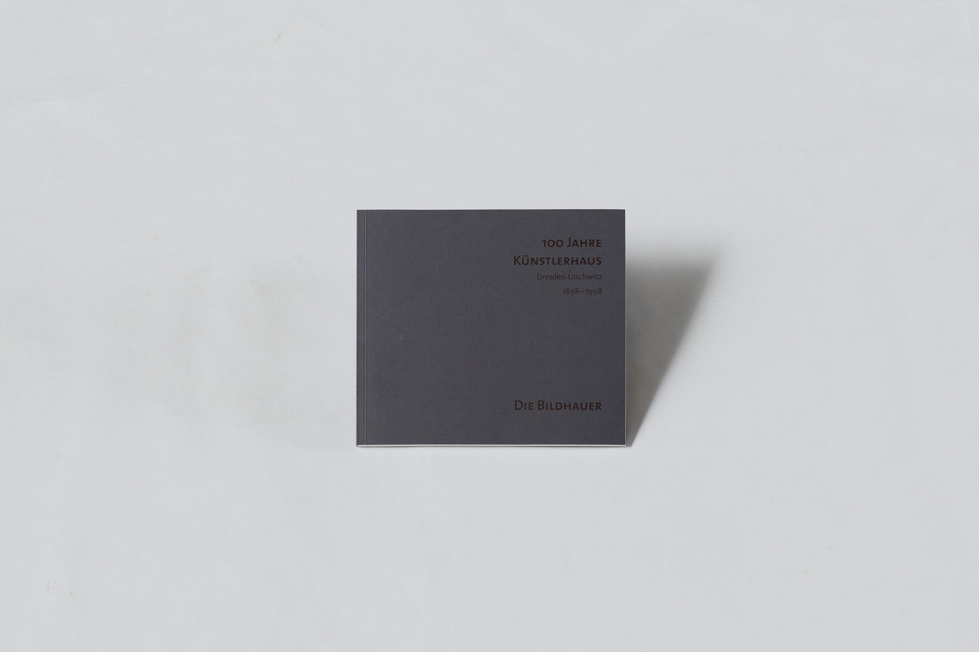 AI generated: The image shows a dark grey book with the title "100 years of the Künstlerhaus" and the subtitle "The sculptors". The book lies on a light-coloured background.