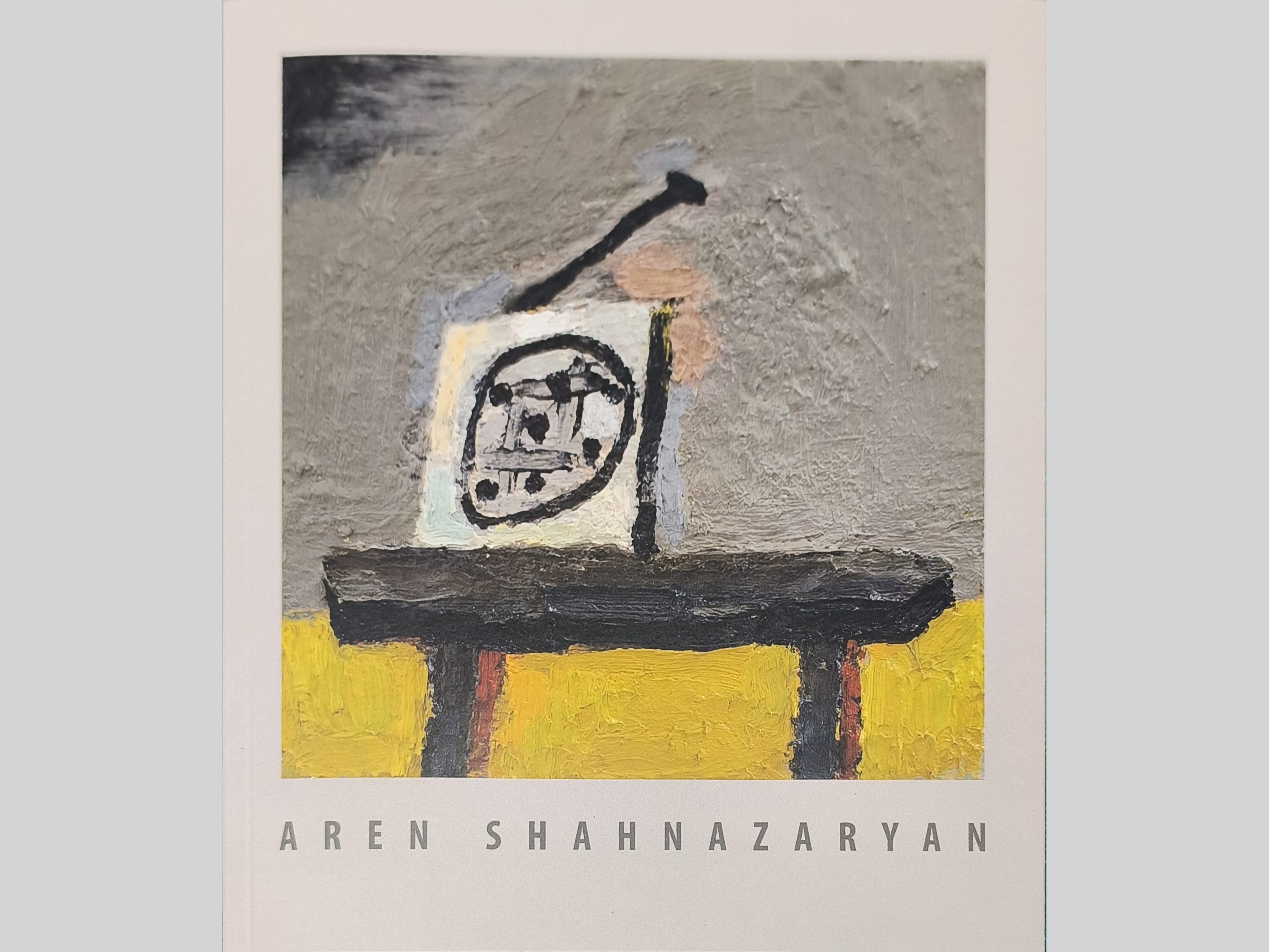 KI generiert: Das Bild zeigt ein abstraktes Gemälde mit kräftigen Pinselstrichen und einer geometrischen Form im Zentrum, die Schwarz auf einer hellen Leinwand darstellt. Der Hintergrund ist in Grautönen gehalten, während der untere Bereich gelbe und orange Akzente hat.