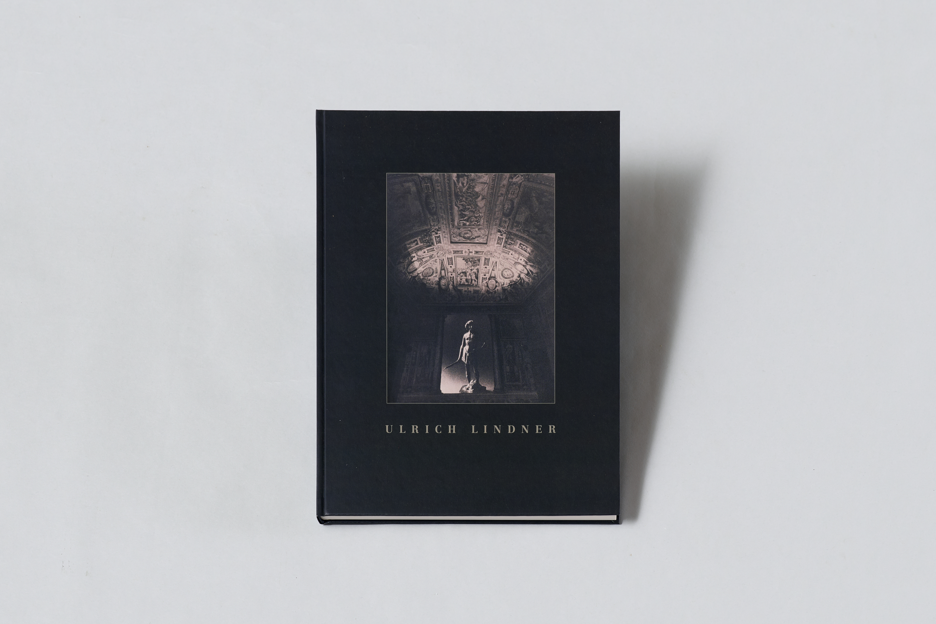 AI generated: The image shows a closed book with a dark cover, on which a photo of an ornately decorated ceiling with a statue is depicted. The name "Ulrich Lindner" can be seen on the cover.